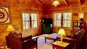 Interior acogedor de una cabaña con paredes de madera, chimenea, televisor y estantería.