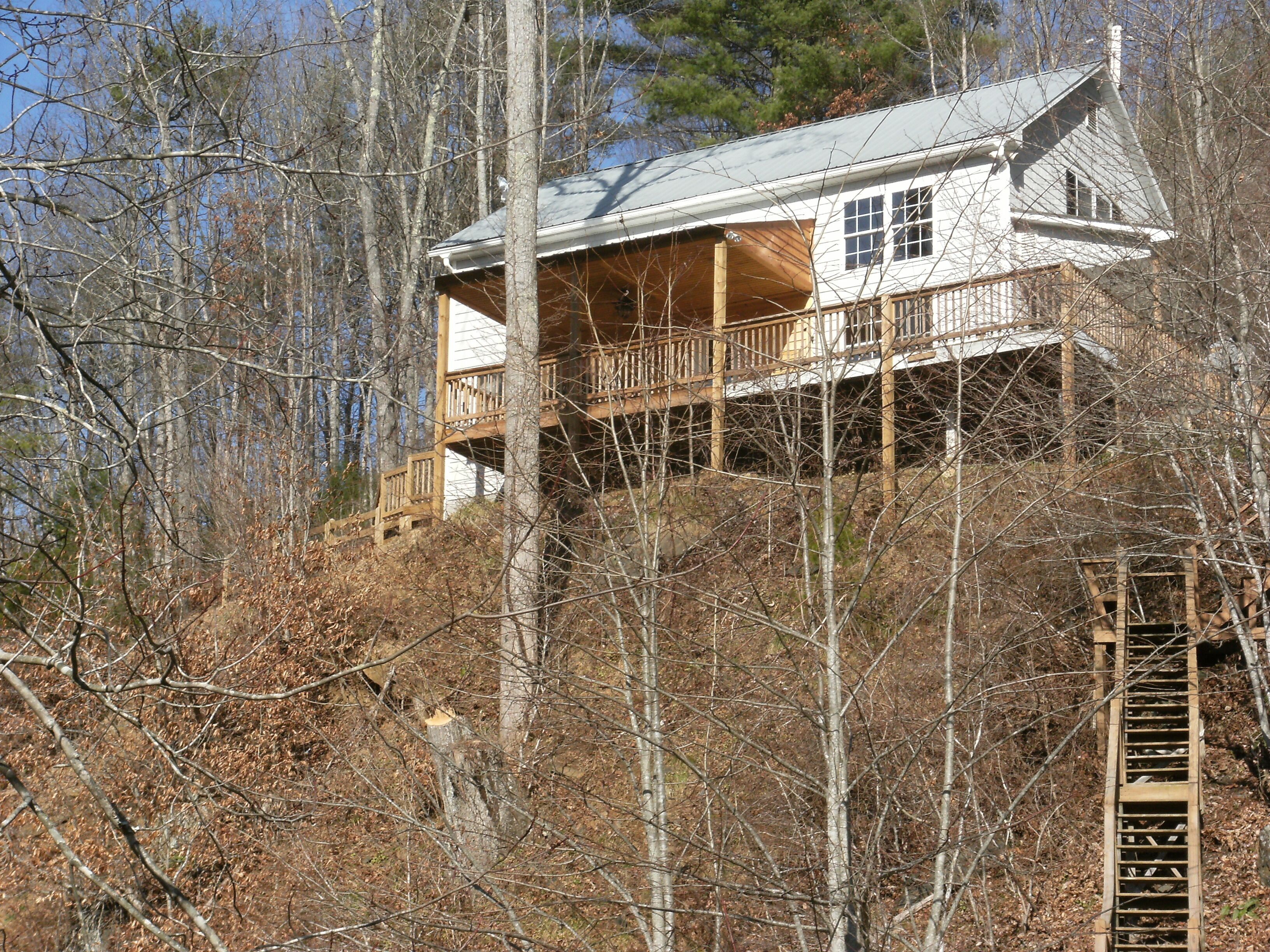 A cabin with a wooden deck and a metal roof, surrounded by trees.