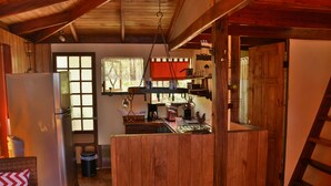 Une cuisine rustique avec des poutres en bois, un réfrigérateur, un évier et une fenêtre donnant sur un paysage agréable.