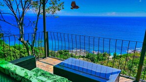 Un balcon avec vue sur l’océan, un canapé vert et une petite table.