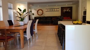 A modern living room with a dining area, a sofa, a coffee table, and a kitchen area with a counter and stools. - 5 Star Luxury Villa with Private pool (Scarborough)