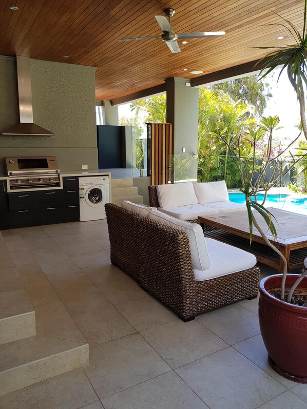 A modern outdoor living area with a sofa, a table, a ceiling fan, a built-in oven, and a washing machine.