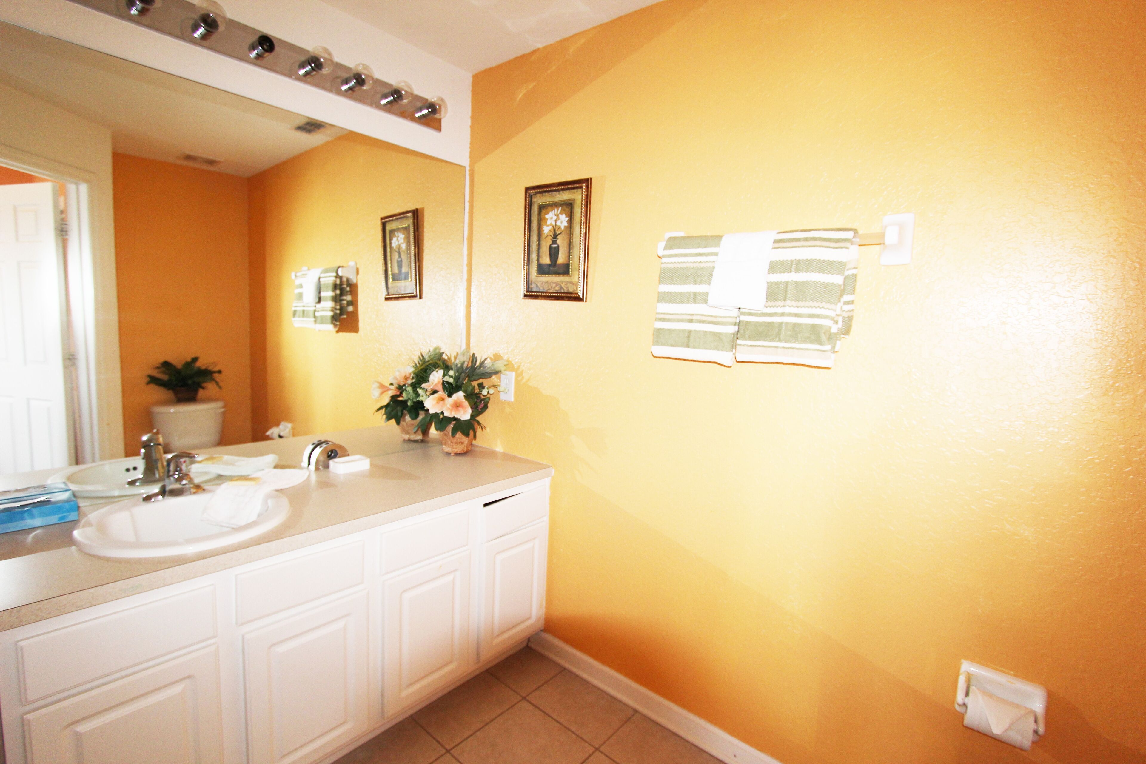 A bathroom with a white vanity, a sink, and a mirror. There are two framed pictures on the wall and a towel rack.