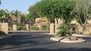 A gated entrance with a paved driveway leading to a building with a tiled roof. - Beautiful central Scottsdale location, golf, restaurants  and very convenient. (Scottsdale)