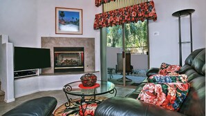 A living room with a fireplace, a television, a sofa with floral cushions, and a glass coffee table. - Beautiful central Scottsdale location, golf, restaurants  and very convenient. (Scottsdale)