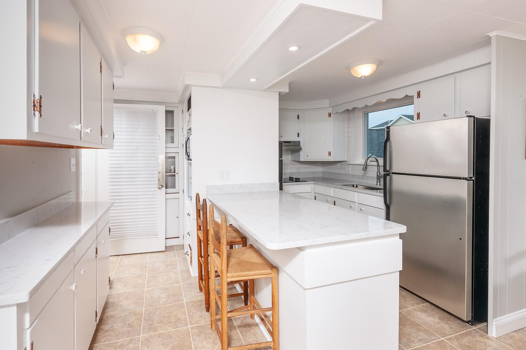 Een moderne keuken met witte kasten, een roestvrijstalen koelkast en een marmeren aanrecht.