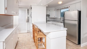 A modern kitchen with white cabinetry, a stainless steel refrigerator, and a marble countertop. - Main House at One Long Beach (York)