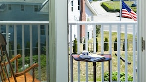 A balcony with a rocking chair and a table, overlooking a residential area with houses and a flag. - Main House at One Long Beach (York)