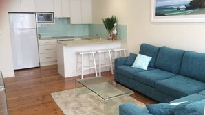 A modern kitchen with white cabinets, a stainless steel refrigerator, and a small island with bar stools. - North Avoca Beach House
200m level walk to beach
4 bedrooms
secure yard (North Avoca)