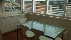 A dining area with a glass table and white chairs, large windows with blinds, and a view of greenery outside. - North Avoca Beach House
200m level walk to beach
4 bedrooms
secure yard (North Avoca)