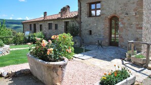 A stone building with a tiled roof, a garden with potted plants, and a clear view of the surrounding landscape.