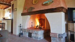 A stone fireplace with a fire, a television, and a wooden cabinet.