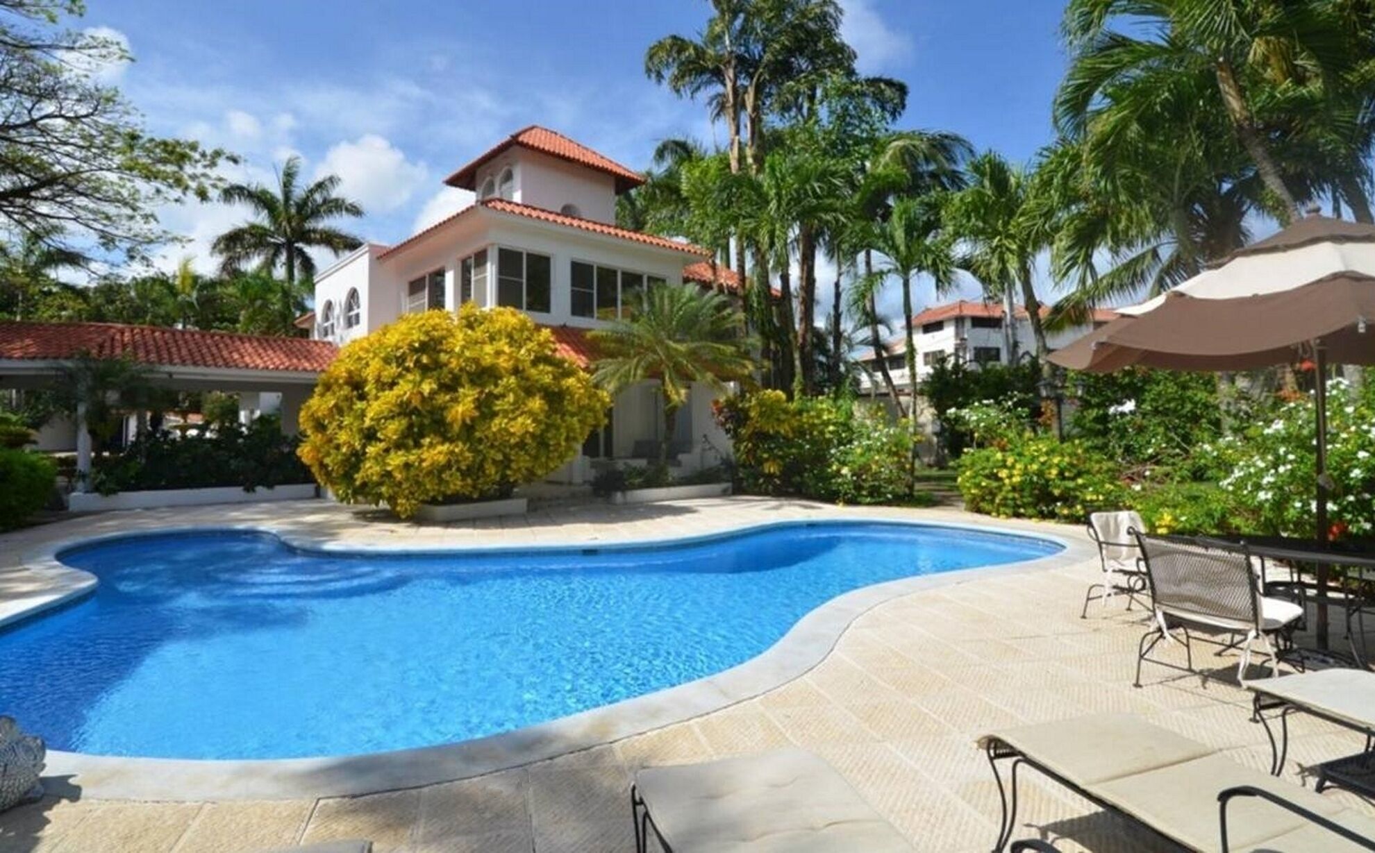 Uma piscina com borda curva, rodeada por um espaço de terraço com mobiliário de exterior.