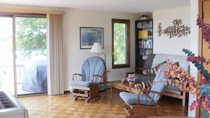 Una sala de estar con piso de madera, un sillón azul, un sofá gris y una estantería.