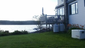 Una casa con terraza y vista a un lago, una estatua y dos tanques de propano grandes.