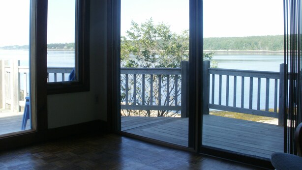 Una habitación con un amplio ventanal corredera que da a una terraza con vistas a un lago y árboles.