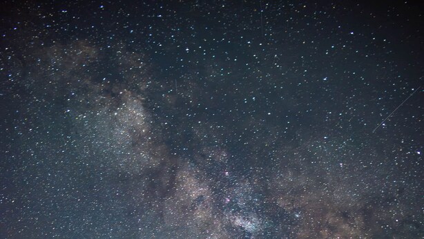 Un ciel nocturne étoilé, avec la Voie lactée au-dessus d’une zone herbeuse où se trouvent deux chaises en bois.
