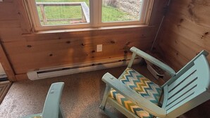 Une pièce avec une grande fenêtre donnant sur une plage, deux chaises avec des coussins à motifs et une petite table.