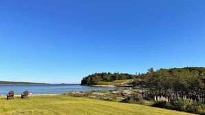 Une vue sur le lac, avec deux fauteuils Adirondack, une pelouse et, au loin, une île boisée.