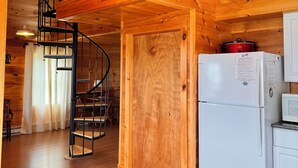 Un intérieur en bois avec un escalier en colimaçon, un réfrigérateur blanc et une porte en bois.