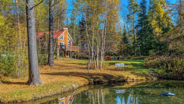 Ein Haus mit rotem Dach, umgeben von Bäumen und einem Teich.