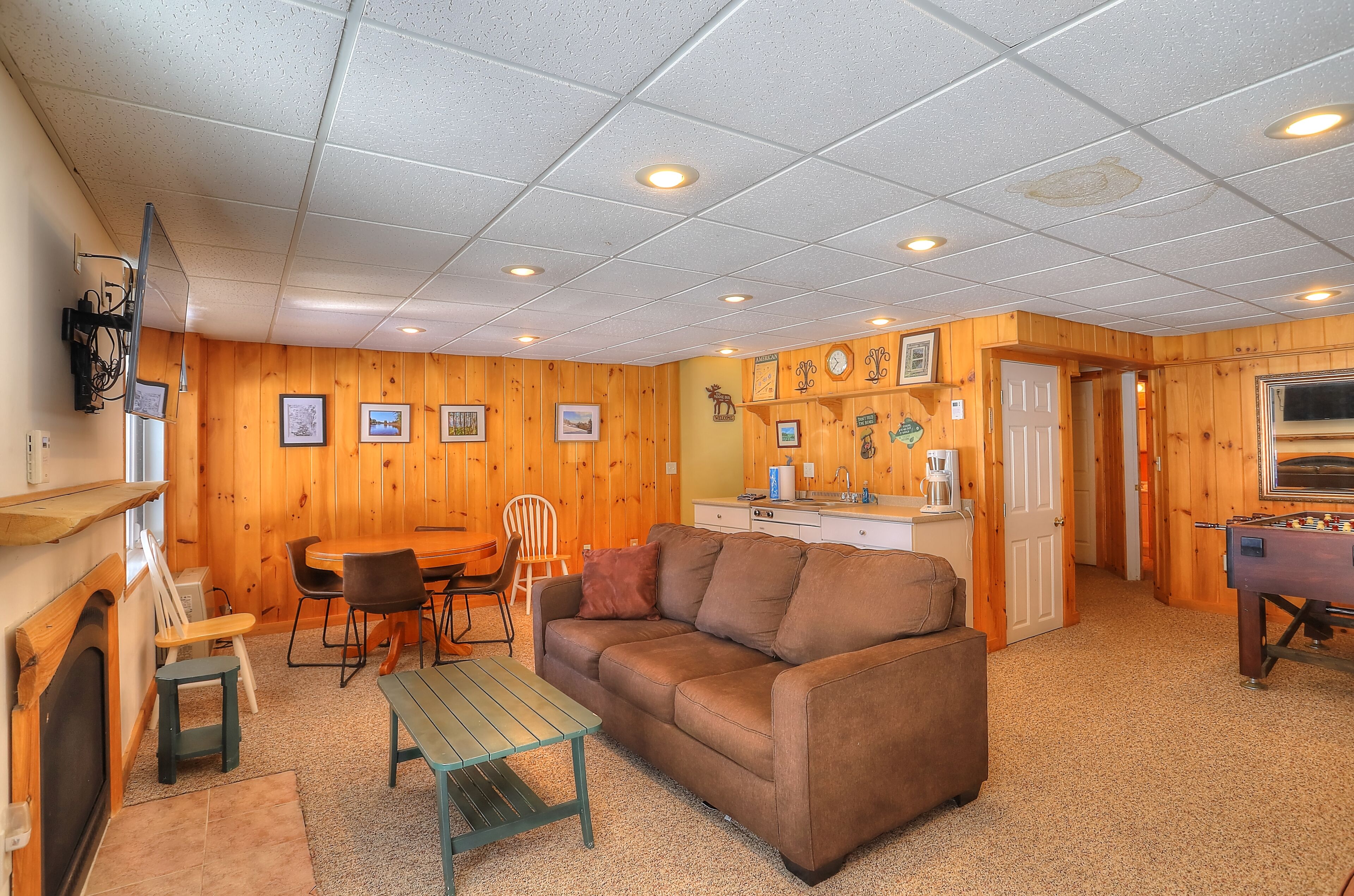 A cozy room with a wooden interior, a sofa, a dining table with chairs, a coffee machine, and a foosball table.