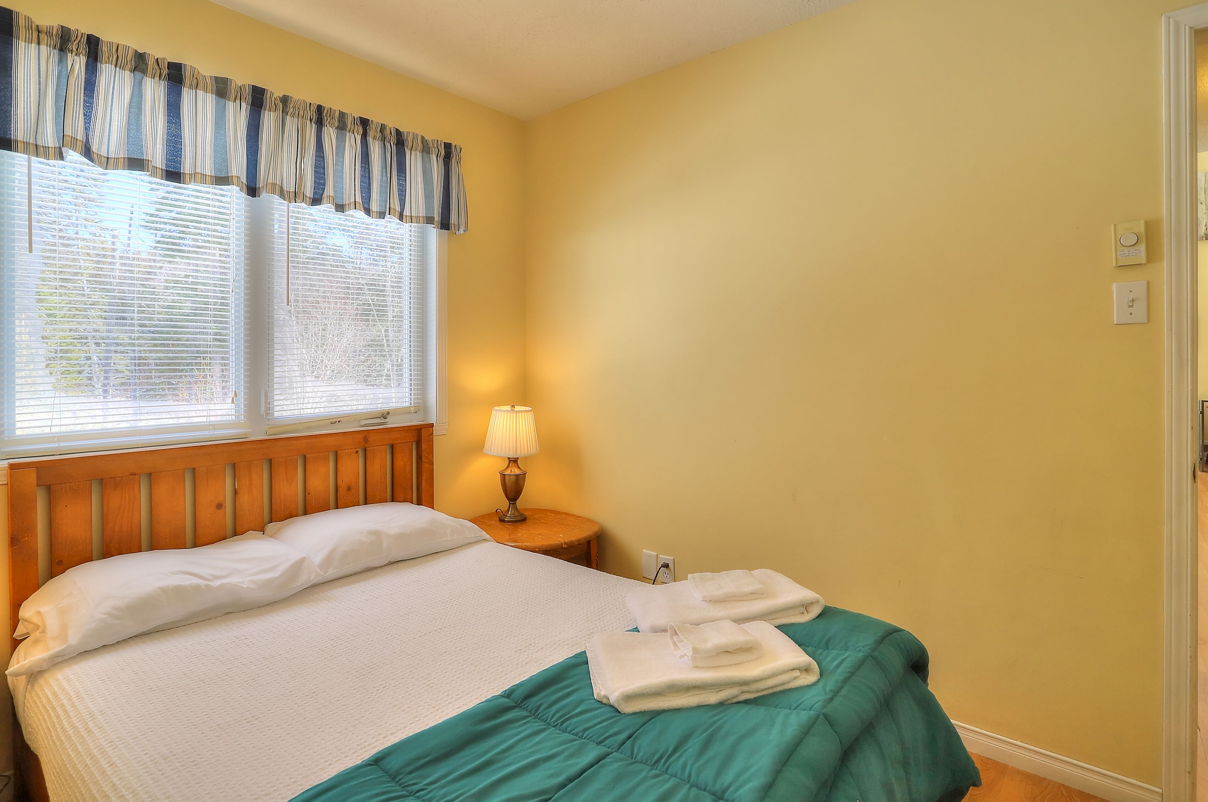 A hotel room with a bed, a nightstand with a lamp, and a window with curtains.