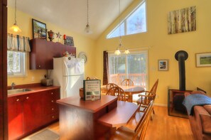 A kitchen with wooden cabinets, a refrigerator, a dining table with chairs, and a large window. - Mahara 1 - Nice home with Rangeley Lake access in the summer (Rangeley)