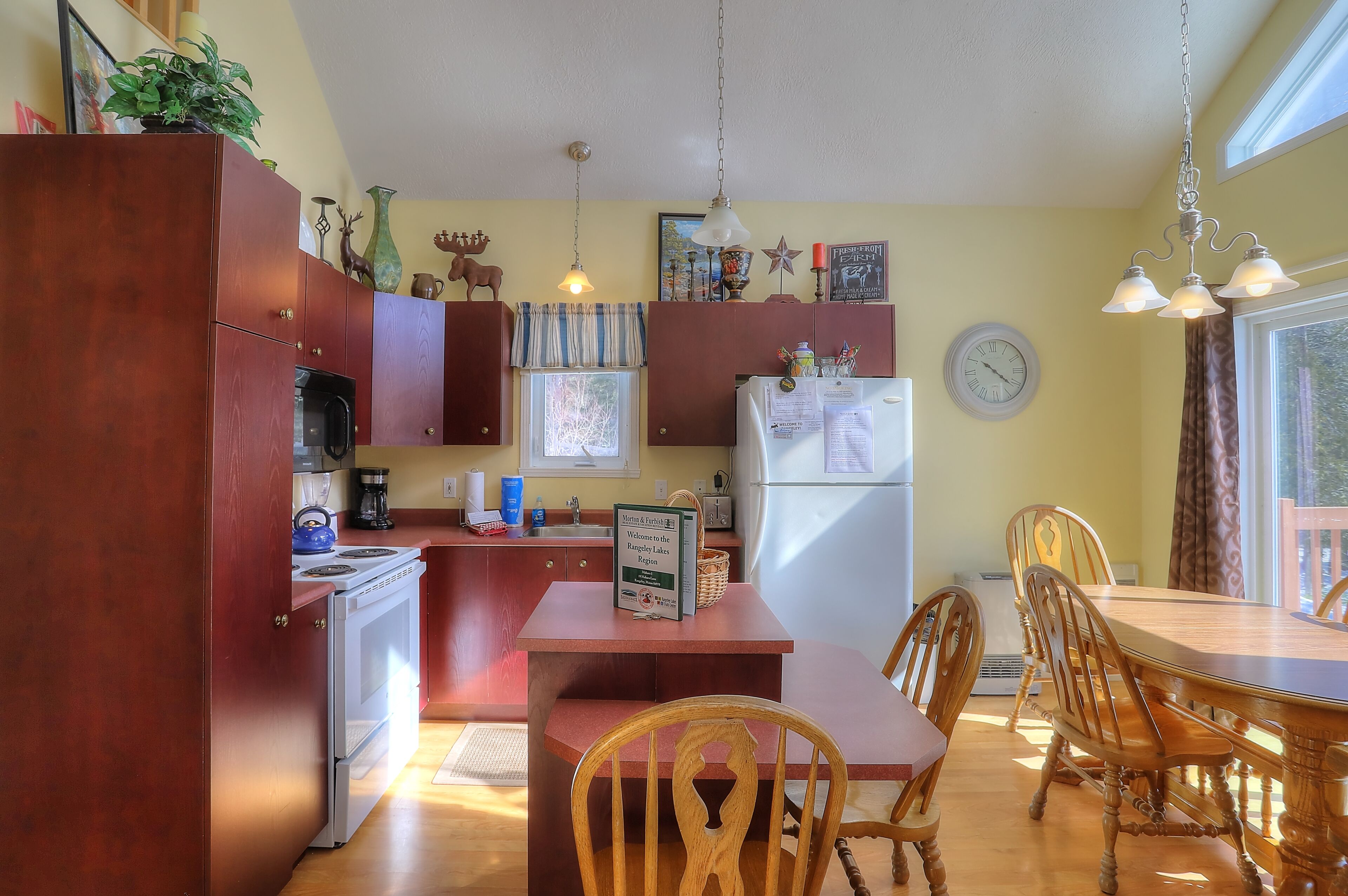 A compact kitchen with wooden cabinets, a refrigerator, a stove, and a dining area with a table and chairs.