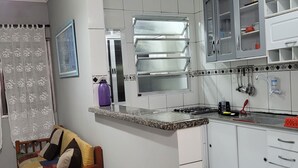 Una cocina compacta con armarios blancos, estufa integrada y una ventana con reja de metal.