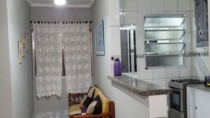 Un espacio habitable compacto con kitchenette, ventilador de techo y cortina estampada.