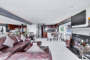 Una sala moderna con sofá de cuero, mesa de comedor y televisor de pantalla plana sobre la chimenea.