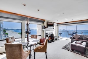 A modern living room with a large window overlooking a beach, a fireplace, and a seating area with a view of the water. - Corner Bayfront balcony, beach, parking, bikes (San Diego)