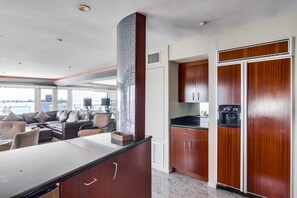 A modern kitchen with dark wood cabinets, a marble countertop, and a view of the sea through large windows.