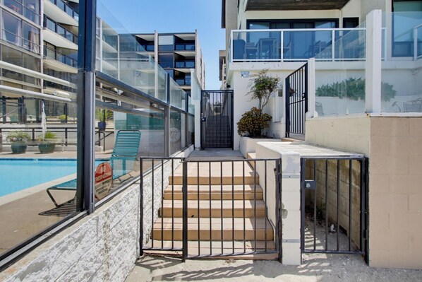 A residential building with a pool, a gated entrance, and a staircase leading to the entrance.