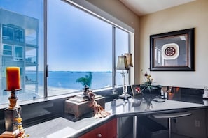 A modern kitchen with a large window overlooking a body of water, a decorative candle, and a framed artwork on the wall. - Corner Bayfront balcony, beach, parking, bikes (San Diego)