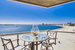 A balcony with a glass table and chairs overlooking a beach and sea. - Corner Bayfront balcony, beach, parking, bikes (San Diego)