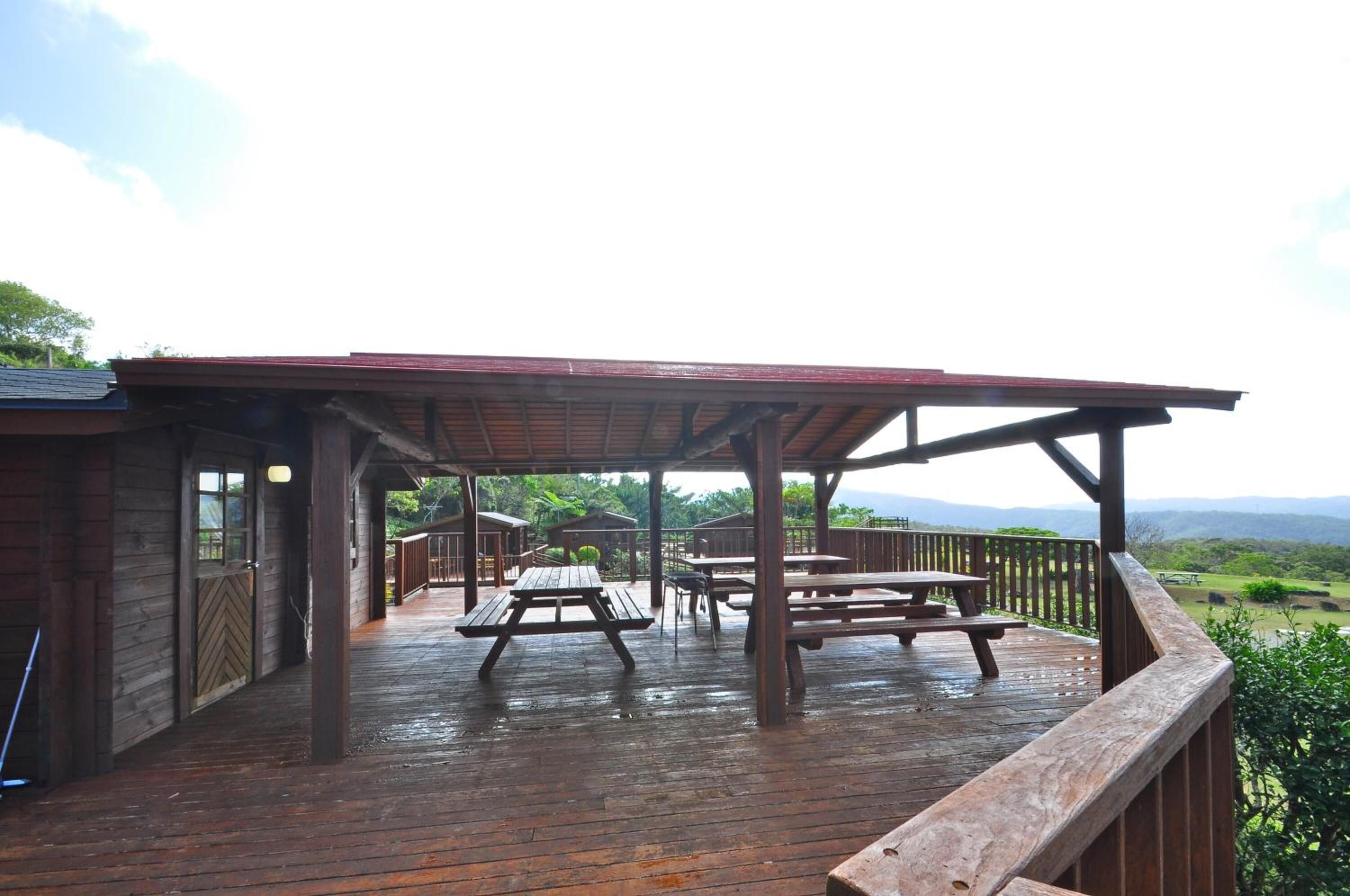 A wooden deck with picnic tables and a covered area, overlooking a scenic landscape.