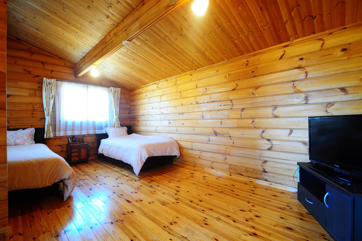 Eine Holzhütte mit Holzwänden und -böden, zwei Betten, einem Fernseher und einem Fenster mit Vorhängen.