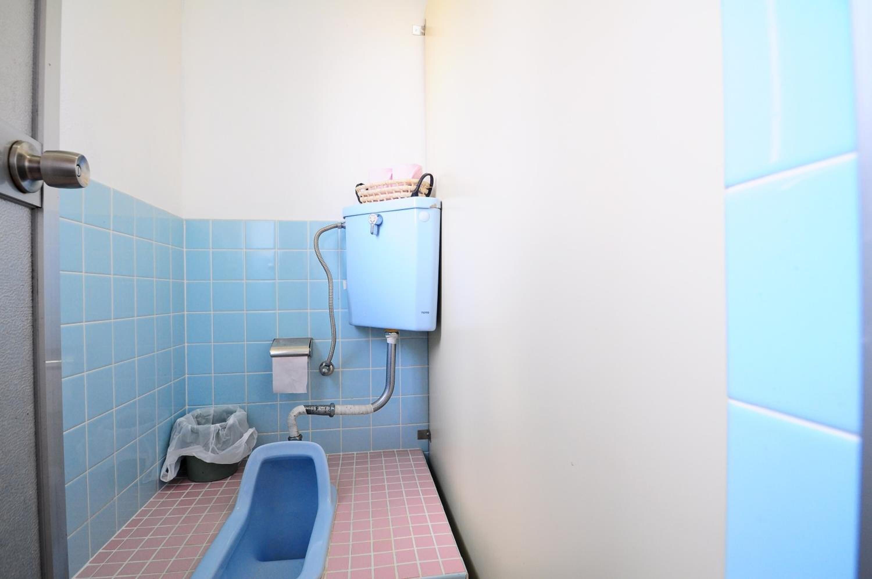 Un baño pequeño con un inodoro azul, un lavamanos y un cubo de basura.