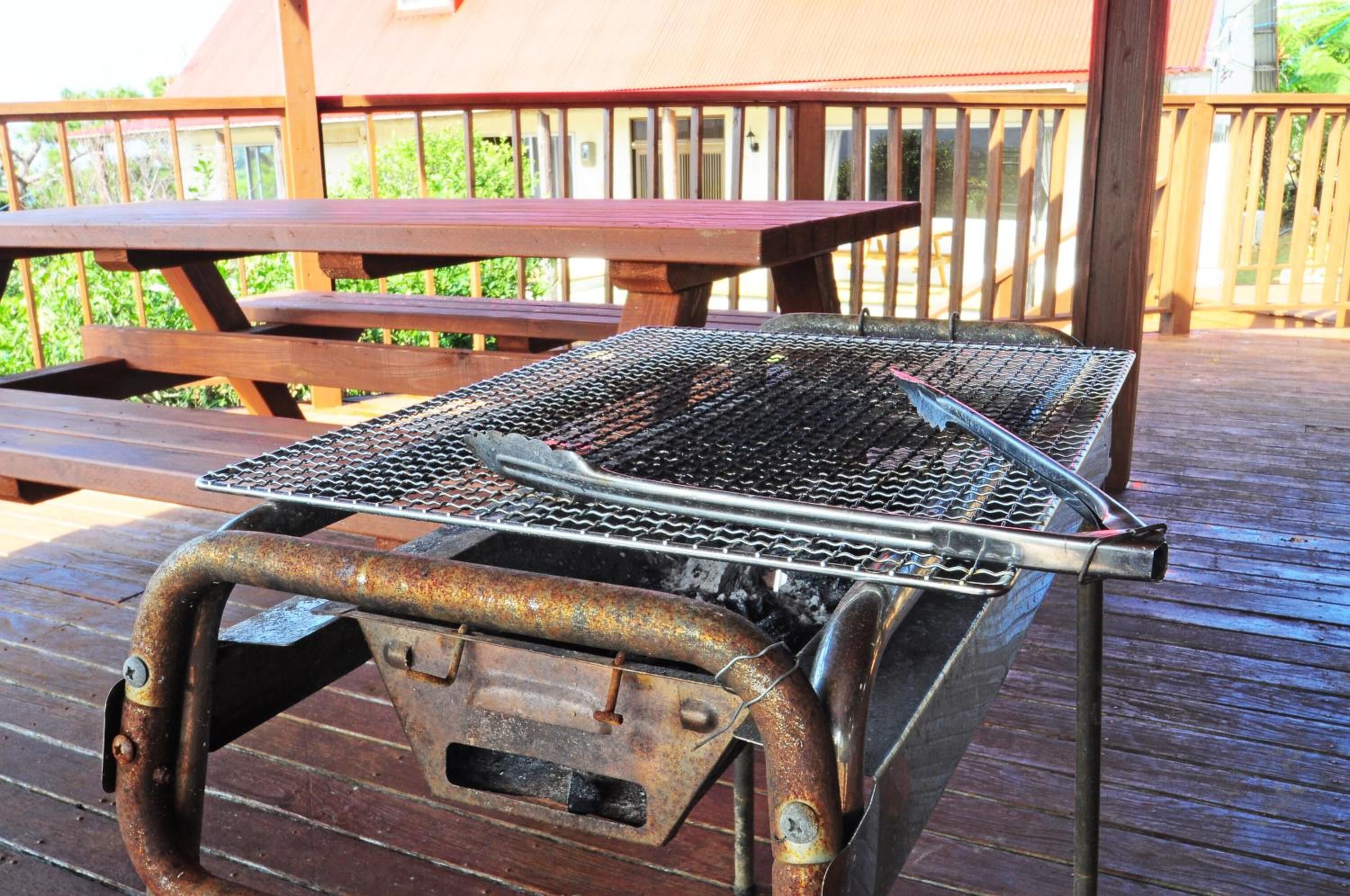 A barbecue grill on a wooden deck with a picnic table in the background.
