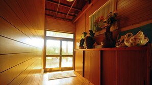 Un interior de madera con una puerta corredera que da a un espacio luminoso, una estantería con adornos y un cuadro en la pared.