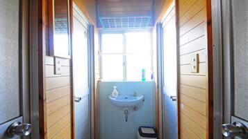 A narrow bathroom with wooden walls, a window, a sink, and a small trash bin.