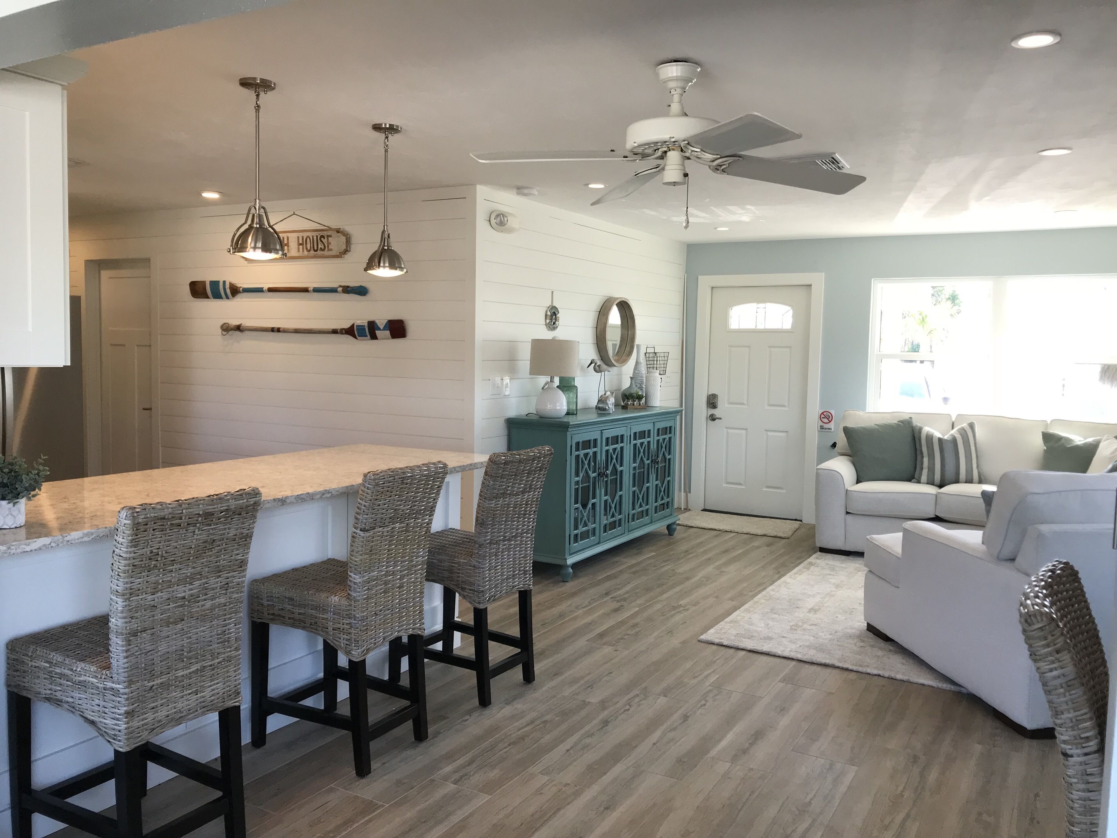 A modern kitchen with a bar area, wicker chairs, a teal cabinet, and a ceiling fan.