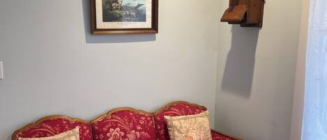 A room with a red floral sofa, a framed picture on the wall, and a wooden object on the wall.