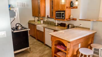 Une cuisine compacte avec des meubles en bois, une cuisinière à gaz, un four à micro-ondes et un petit îlot central avec des tabourets.