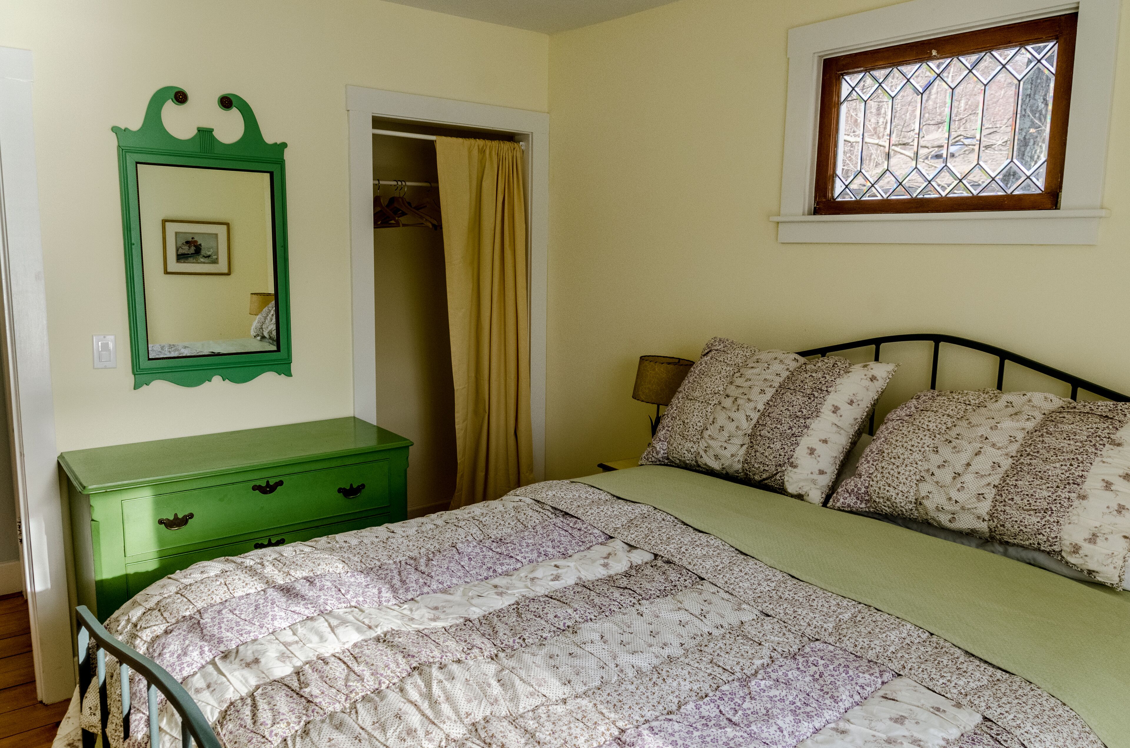 Une chambre à coucher avec un lit, une commode verte, un miroir, une fenêtre et une porte.