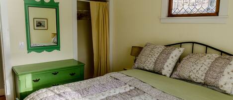 Une chambre à coucher avec un lit, une commode verte, un miroir, une fenêtre et une porte.