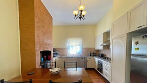 Een keuken met een eettafel, stoelen, een kroonluchter en een koelkast.