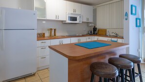Een keuken met witte kastjes, een magnetron, een koffiezetapparaat en een houten kookeiland met krukken.